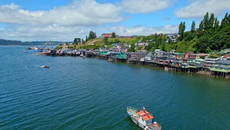 colorful castro stilt houses on chiloe island with a boat cruising, aerial view