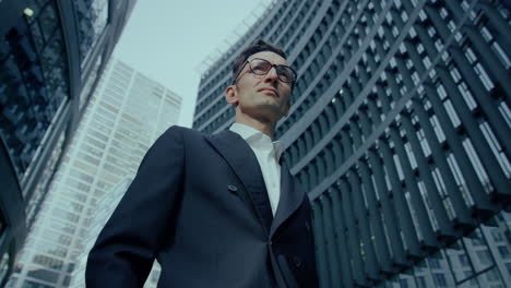 finance manager wearing suit and glasses standing outdoors in front of modern building, low angle view