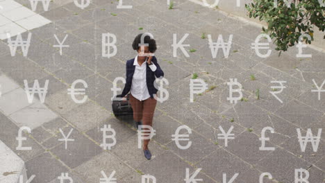 animación de símbolos de moneda sobre una mujer de negocios afroamericana hablando con un teléfono inteligente en la calle