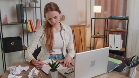 sad young woman working at home office crumples throwing heets of paper with bad ideas and mistakes