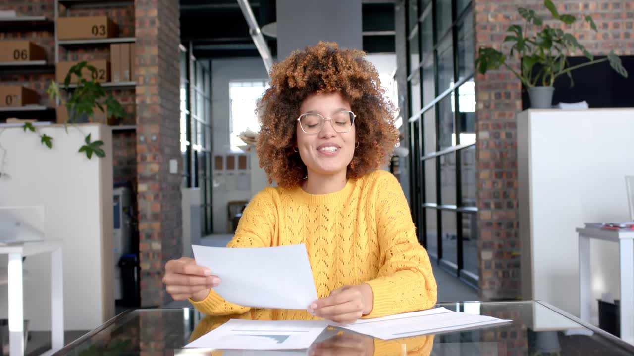 Happy biracial casual businesswoman having video call with documents at office, slow motion