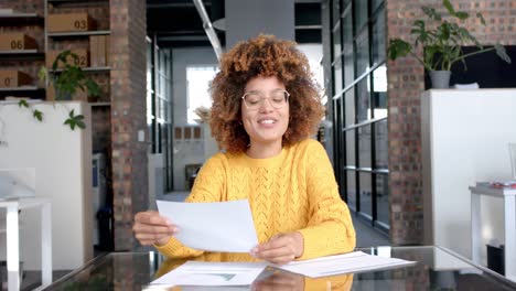 Happy-biracial-casual-businesswoman-having-video-call-with-documents-at-office,-slow-motion