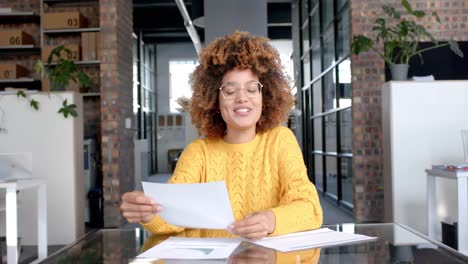 feliz mujer de negocios casual biracial haciendo una videollamada con documentos en la oficina, cámara lenta