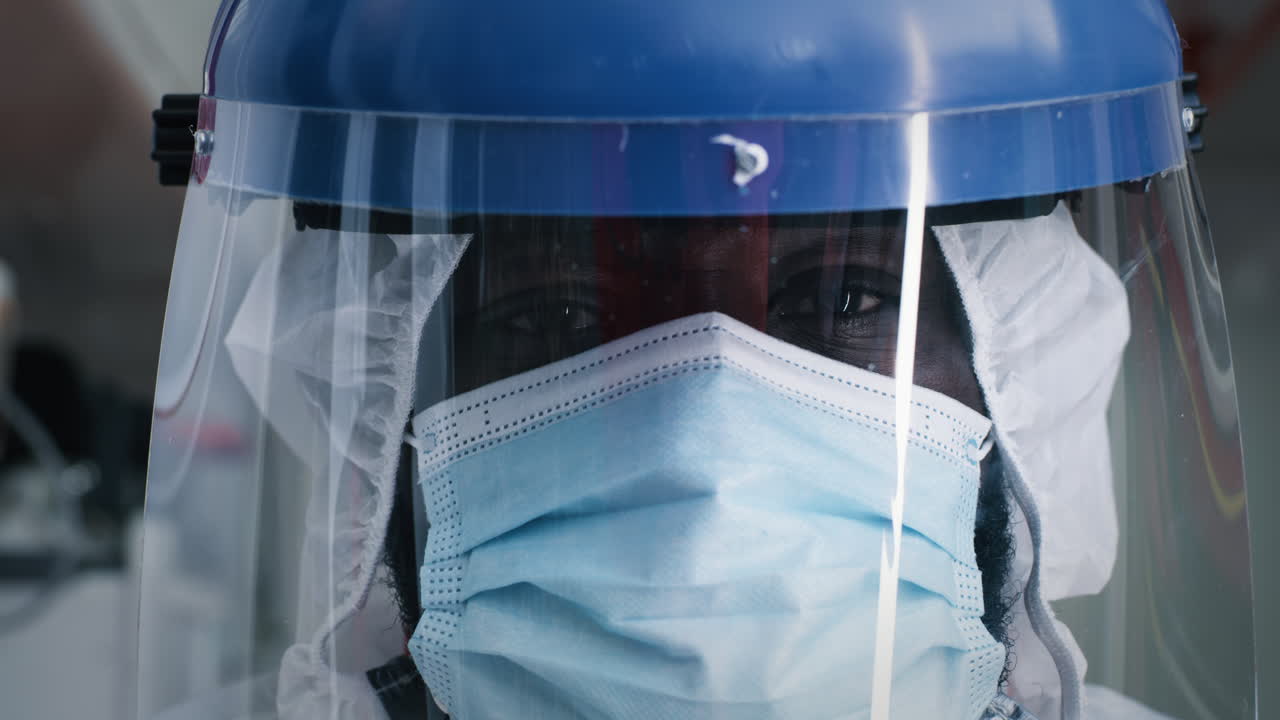 tired Black Doctor in Face Shield and Mask Closeup Exhausted African American Paramedic in Protective Face Shield and Mask Looking at Camera and Blinking Slowly while Working in Emergency Medicine Service