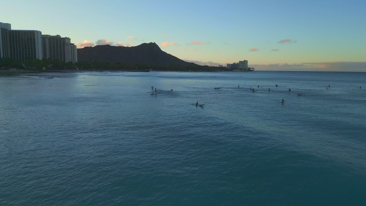 Scenic panoramic drone parallax shot of surfers riding waves in Waikiki Beach, hawaii at sunset