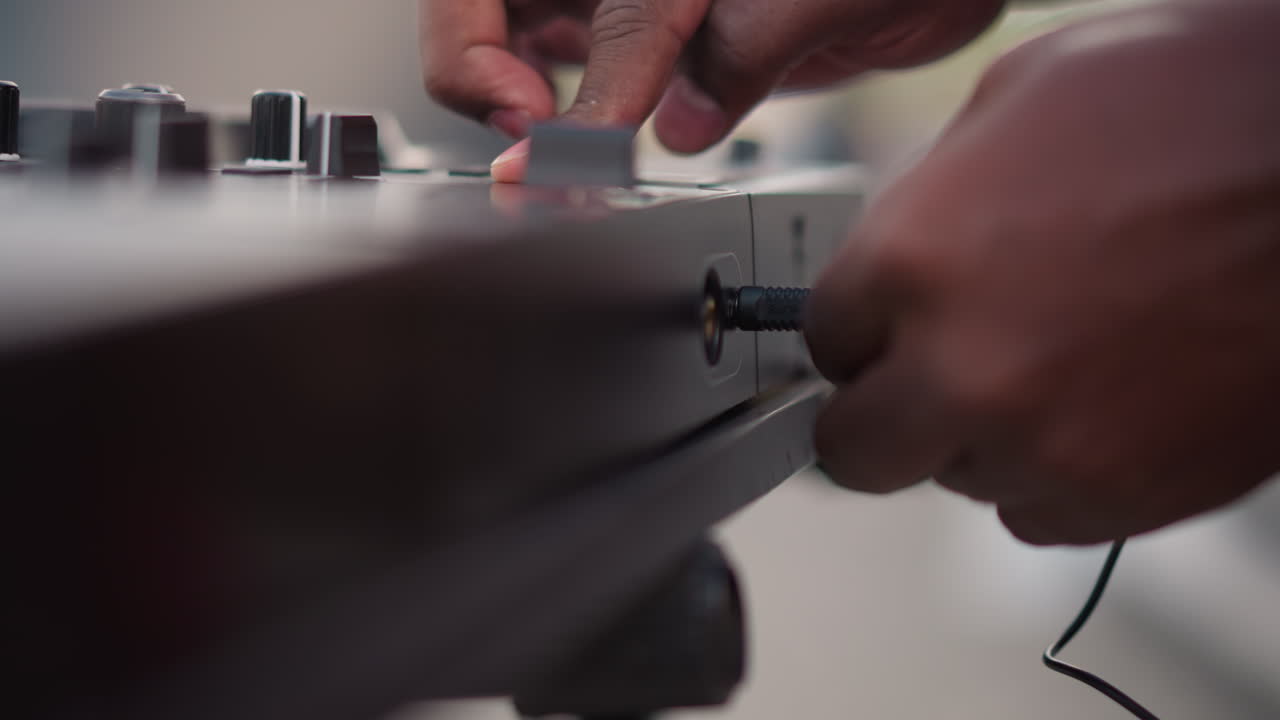 closeup hands plugging cable into mixer street DJ preparing for outdoor gig tight shallow depth of field highlights jack, knobs, fader while fingers connect and adjust levels intimate urban