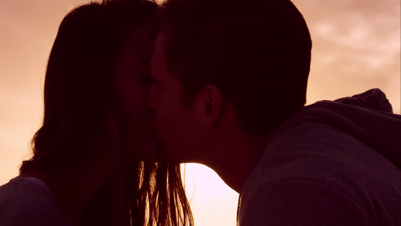 Felice coppia innamorata che si bacia al tramonto, mostrando intimità emotiva, toccandosi, abbracciandosi e coccolandosi.