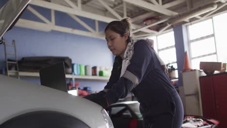 Mecánica-Femenina-Usando-Una-Computadora-Portátil-E-Inspeccionando-El-Automóvil-En-Una-Estación-De-Servicio-De-Automóviles