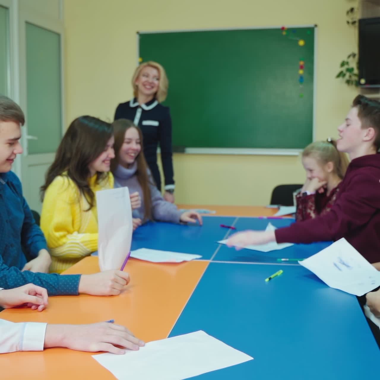 Teen students at school. Happy children sitting in the classroom and throw papers up. Students enjoys the time together. Papers flying in the class. Slow motion.