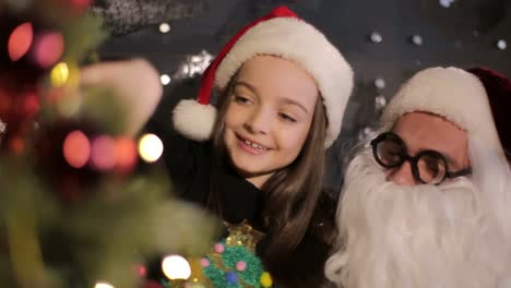 a little girl sits by the christmas tree and opens a christmas present a little girl sits by the christmas tree and opens a christmas present christmas gifts gifts under the new year tree the child opens a gift celebrating christmas and new year