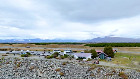 aerial footage captures a serene landscape with scattered buildings and vehicles near lake pukaki under a cloudy sky
