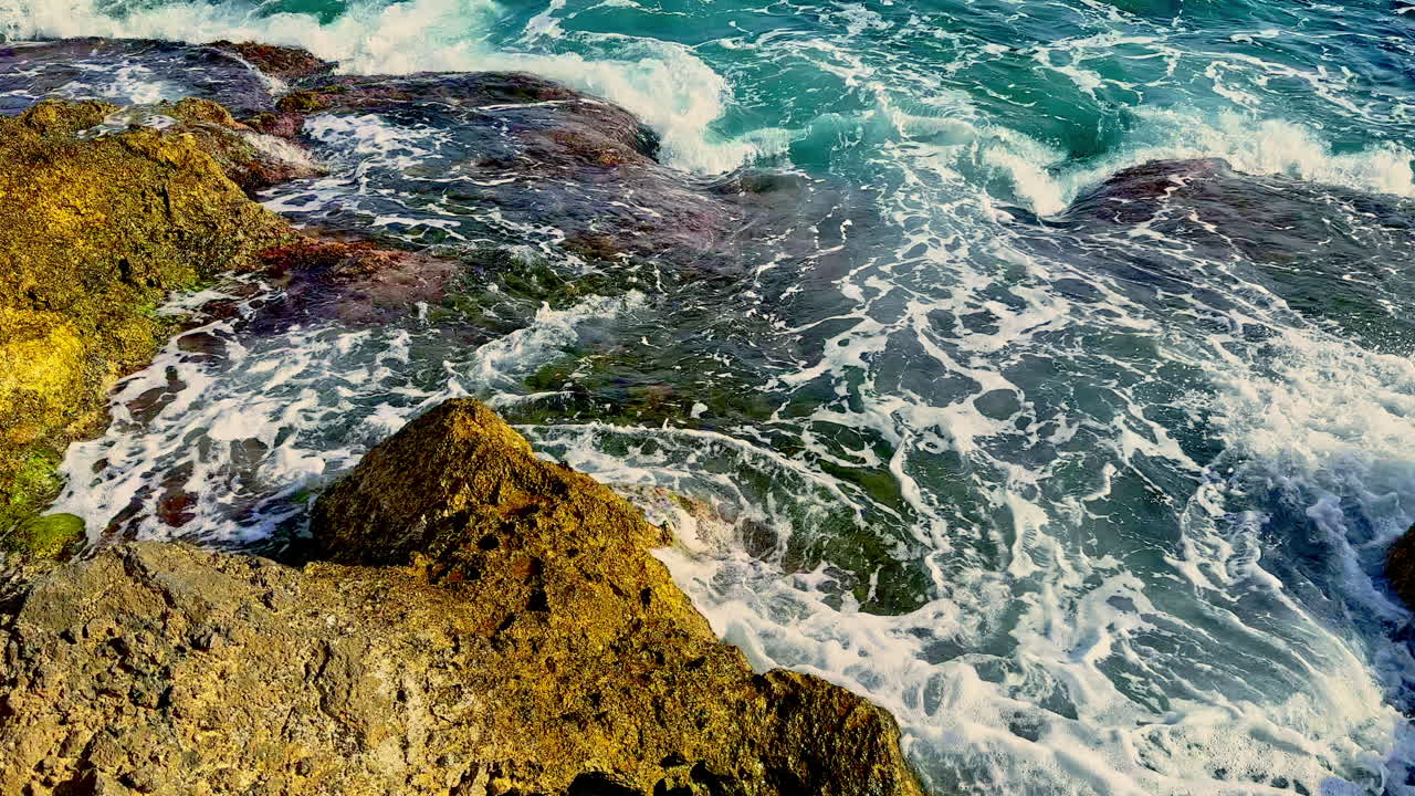 Felsstrand, an dem sich Wellen brechen. Blaue Meereswellen umspülen die Steine. Meeressteine.