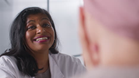 smiling female doctor or oncologist giving good news at meeting with woman patient wearing headscarf undergoing chemotherapy treatment for breast cancer in hospital