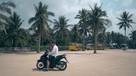 guy sits on girl stands by scooter on square against palms