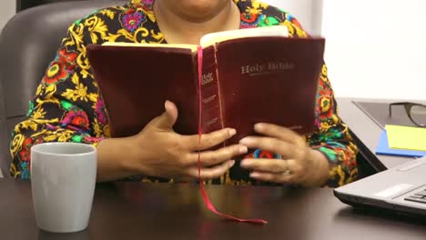 mujer negra vestida con pantalones vintage leyendo la biblia en el escritorio en el trabajo en la oficina, taza de café, nueva normalidad