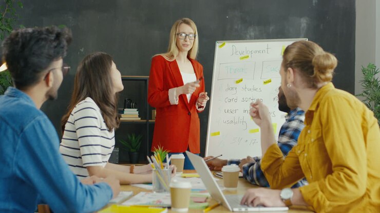 Young Woman Explaining Business Strategy And Development With A Blackboard To Multicultural Entrepreneurs Group In The Office