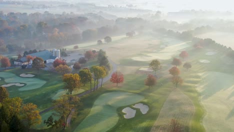 Filmische-Hohe-Luft-Zeigt-Wartungsscheune-Auf-Dem-Golfplatz-Bei-Sonnenaufgang,-Frost-Und-Nebel-Im-Herbstsonnenlicht