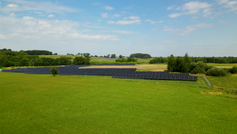 Aerial-solar-panels-farm-in-the-middle-of-green-meadow,-blue-sky-with-clouds-in-background,-renewable-energy-in-Poland