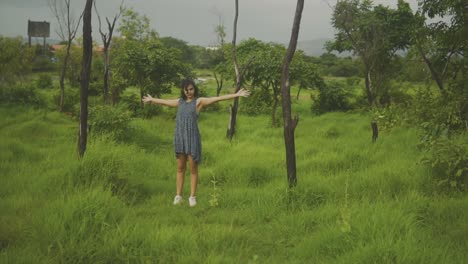 tan-woman-in-dress-holding-arms-outstretched-wide-in-orchard-field,-slow-motion-rack-focus