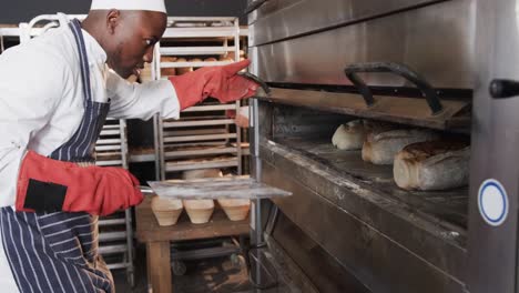 african american male baker working in bakery kitchen, taking bread out of oven, slow motion