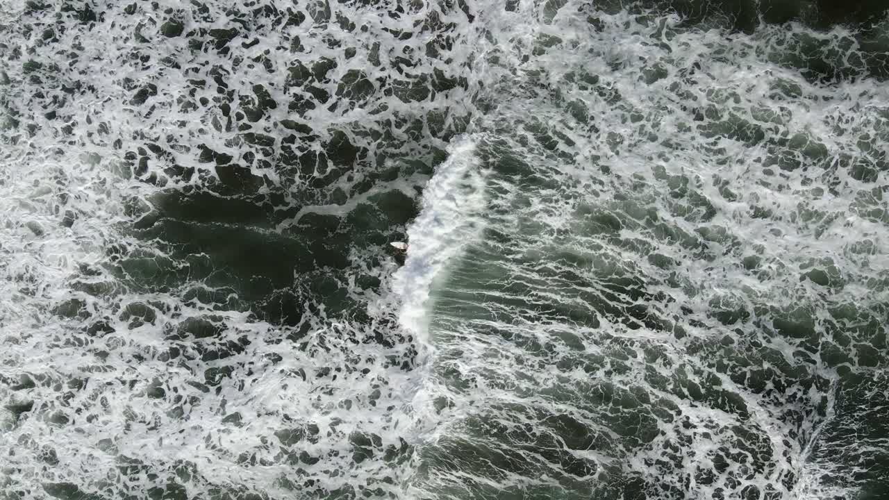 Drone pulls away from lone surfer to reveal vast textured waves