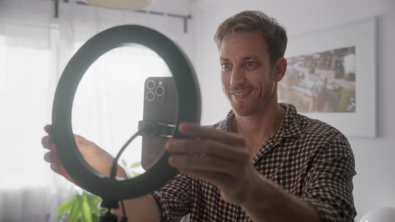 Vlogger or social media influencer is setting up smart phone on ring light stand. Starting recording session or live streaming webinar in home studio or home. Amateur famous online personality talking