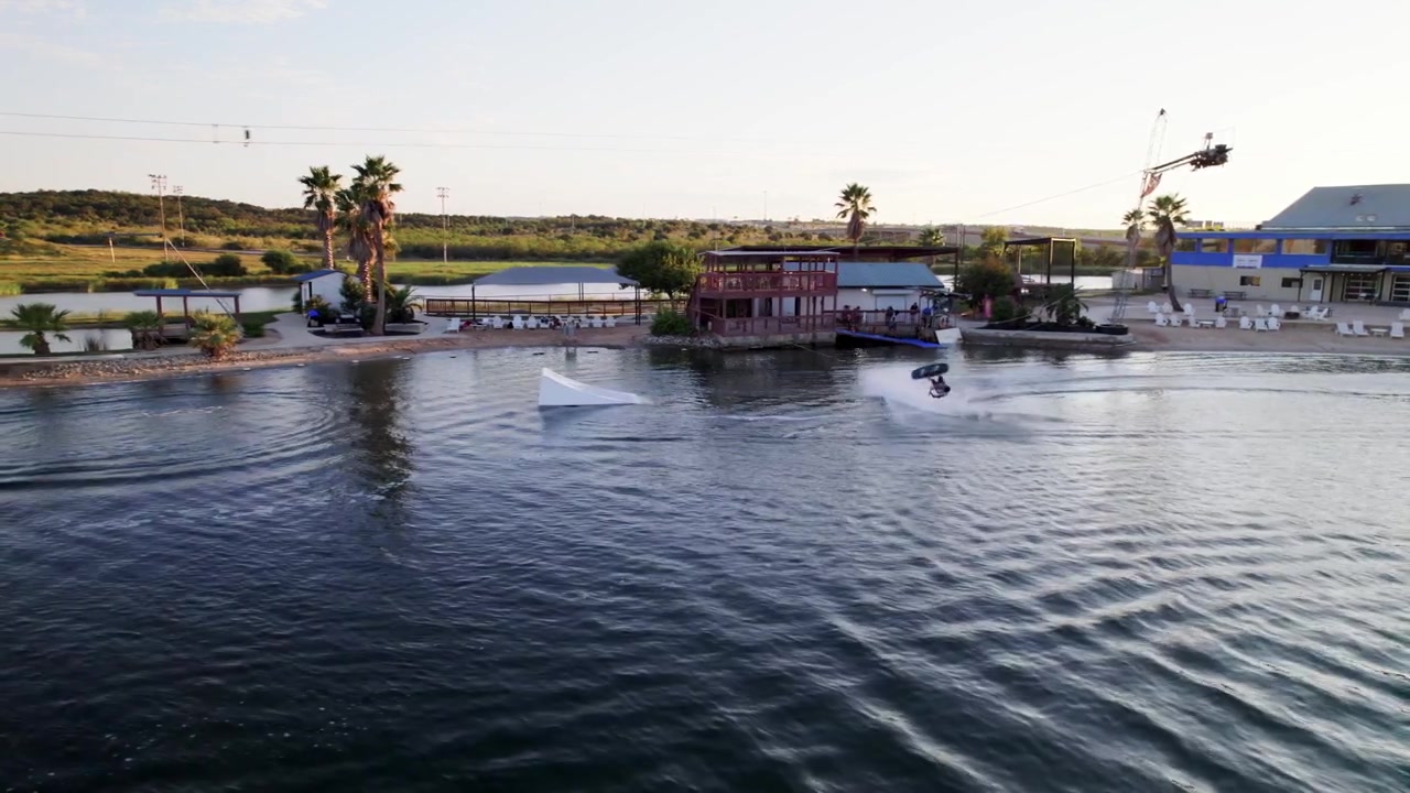 Flygvy över en person som åker wakeboard i en kabelpark vid solnedgången