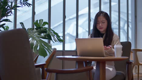 Una-Joven-Asiática-Decepcionada-Y-De-Mal-Humor-Trabajando-En-Línea-En-Su-Computadora-Portátil-Desde-La-Cafetería