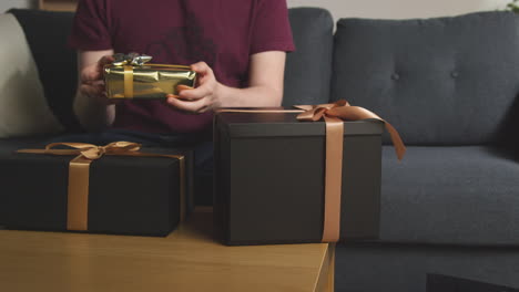 primer plano del hombre abriendo regalos envueltos en la mesa en el salón en casa