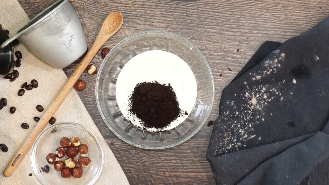 A delicious dessert, Coffee Hazelnut Cream Tart. Made with espresso powder, chocolate crust and loaded with crushed hazelnut. Adding espresso powder to the clear mixing bowl on a wooden table