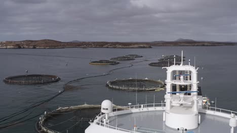 ascending drone shot of the bridge of a well-boat anchored by a fish farm