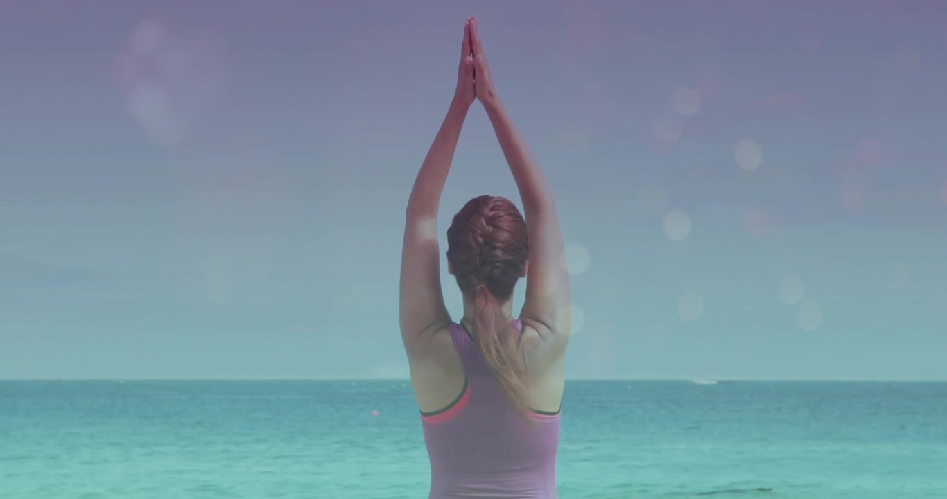Donna adulta che inizia un allungamento yoga estendendo le braccia verso l'oceano turchese, raggiungendo il benessere