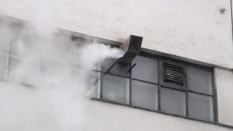 white smoke coming out of an exhaust vent from a building facade with tiny windows