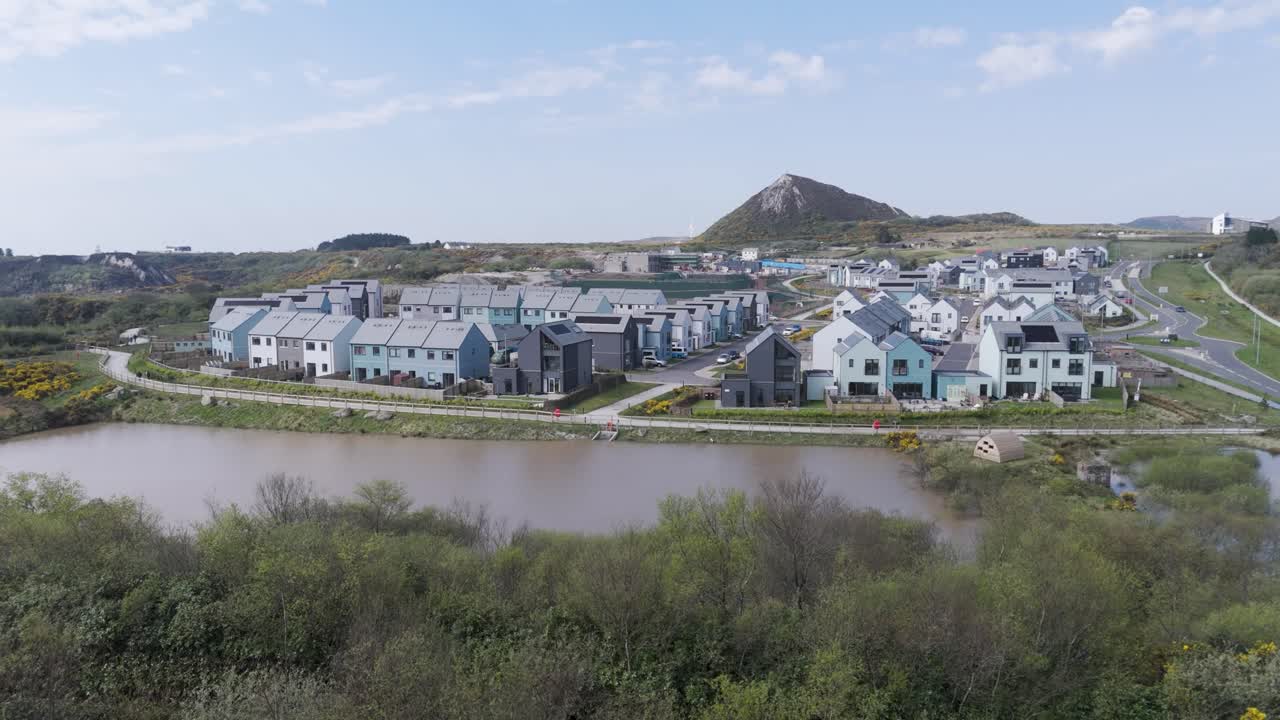 Aerial sweep of sustainable waterfront housing with solar roofs, blue and white facades, curving lanes, and landscaped canal banks in an eco-focused urban regeneration zone