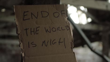 End-of-the-world-handwritten-sign-pinned-to-wall-with-old-building-and-windows-background