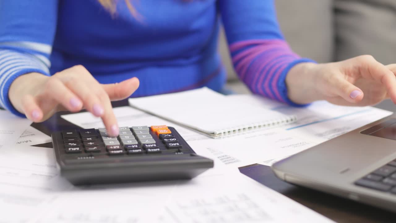 mujer usando calculadora para calcular facturas domésticas en el hogar, haciendo papeleo para pagar impuestos