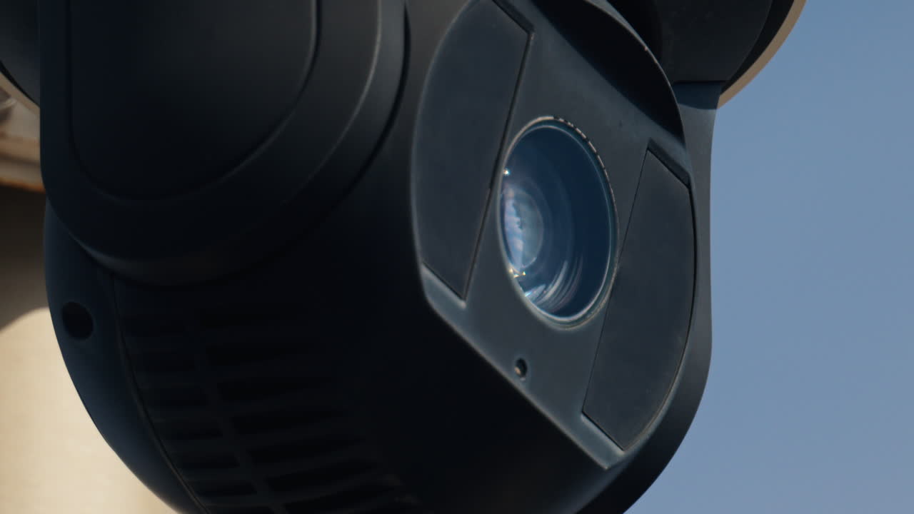 Close up of a round, black surveillance camera mounted on a white pole with the sky on the background
