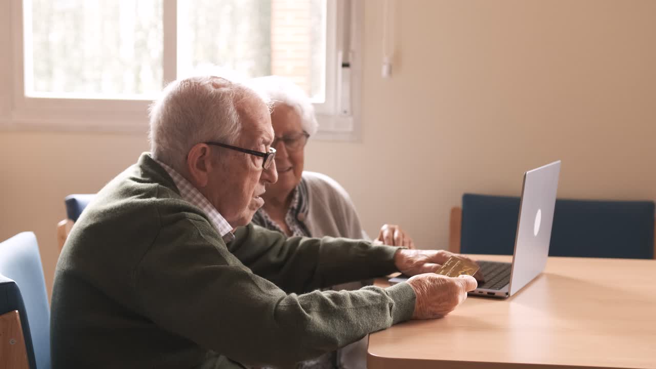 Happy elderly man and woman using laptop and credit card at nursing home
