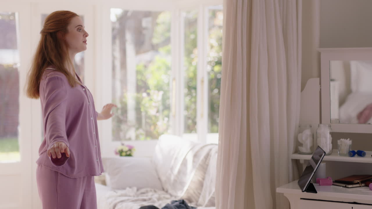 아름다운 젊은 여성이 침실에서 발레 춤을 연습하고 주말 아침에 파자마를 입고 춤을 연습합니다.