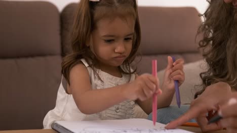 mother teaching daughter to draw in book with felt pens at home