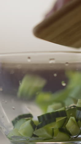 pouring juicy cucumber slices into glass bowl from board cooking healthy salad on table in light kitchen extreme close view slow motion