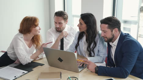 a young work team composed of two women and a man discusses financial matters around a laptop at a business meeting.