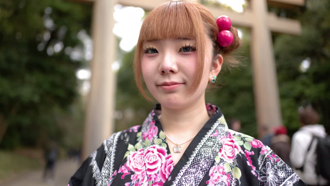 Una donna in yukata floreale sta davanti a un torii di legno a Tokyo.