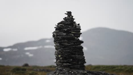 a dark stone cairn in the bleak northern landscape. misty snow-covered mountains in the background. parallax shot.