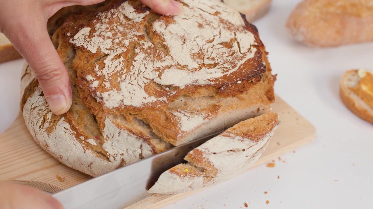Persona che affetta pane di pasta madre fresco e croccante su un tagliere di legno.