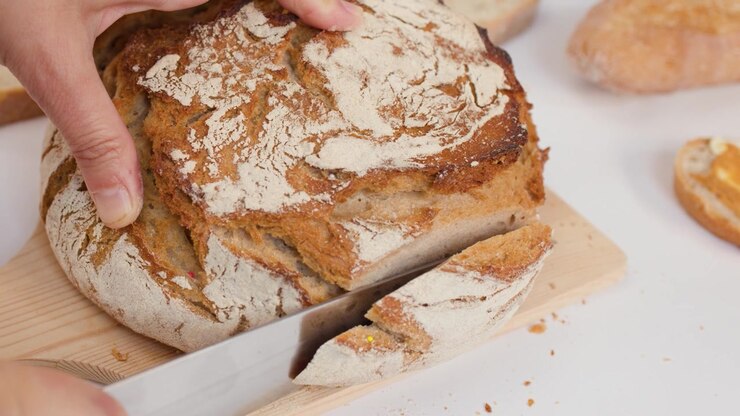 Person Slicing Fresh Crusty Sourdough Bread on a Wooden Board