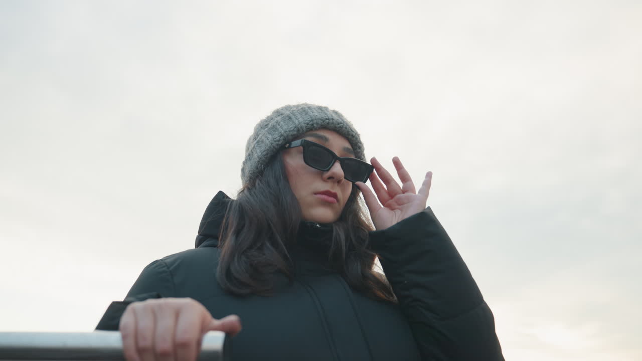 Park stairs portrait with dance stride, woman in puffer coat descending metal steps and adjusting sunglasses, assertive posture, cool overcast light, gritty urban backdrop and modern city vibe