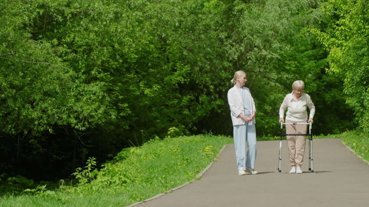 공원 에서 보행기 를 사용 하는 노인 여자 를 지원 하는 여자