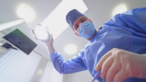 portrait of a dentist in medical uniform. doctor in mask customizes lamp before teeth treatment in modern dental office. view from below.