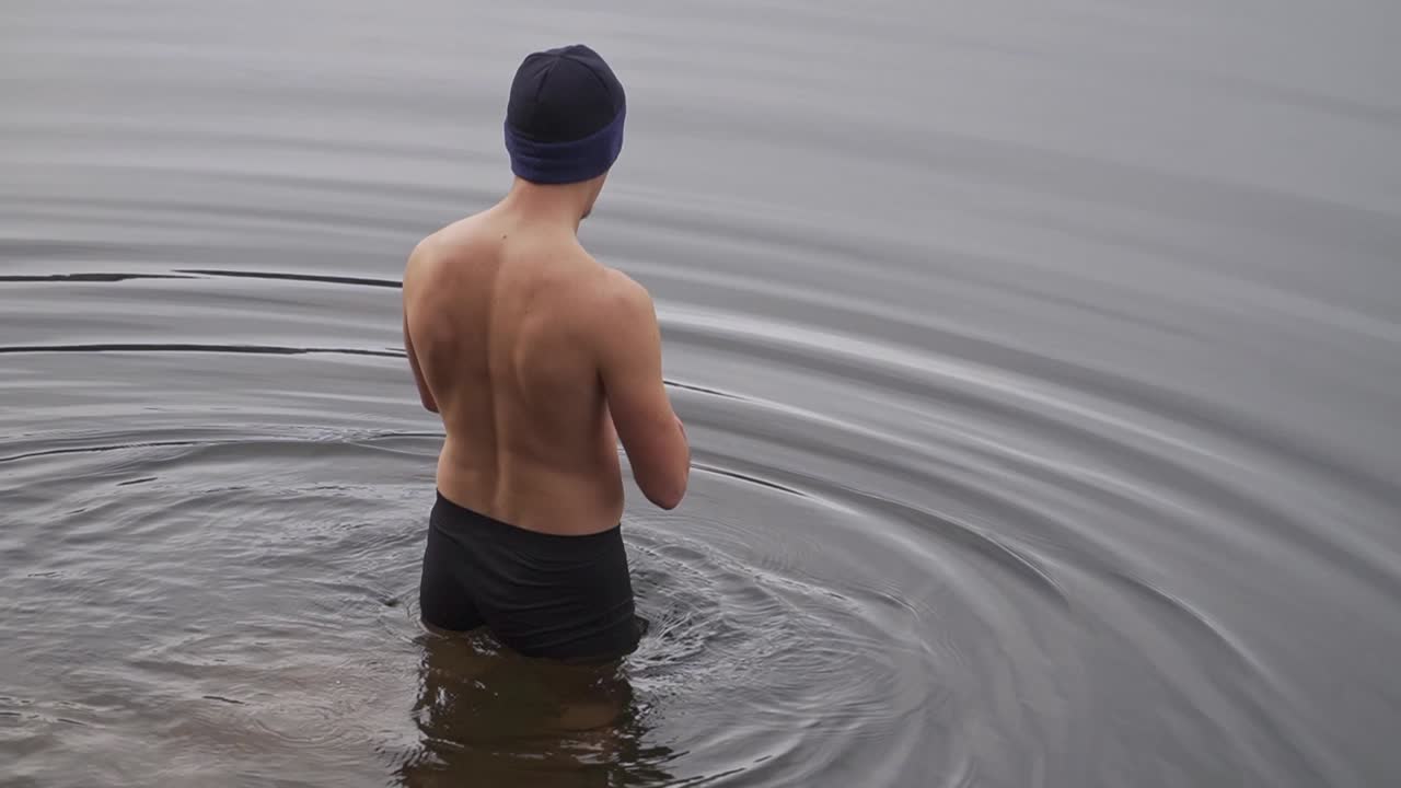 Man walking into cold water wearing only swimming trunks and knit cap. Onsen, cold water therapy, polar plunge concept.